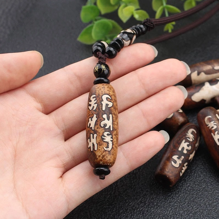 Close-up hand-held view of Om Mani Padme Hum Dzi bead Buddhist necklace showing Sanskrit mantra carving detail