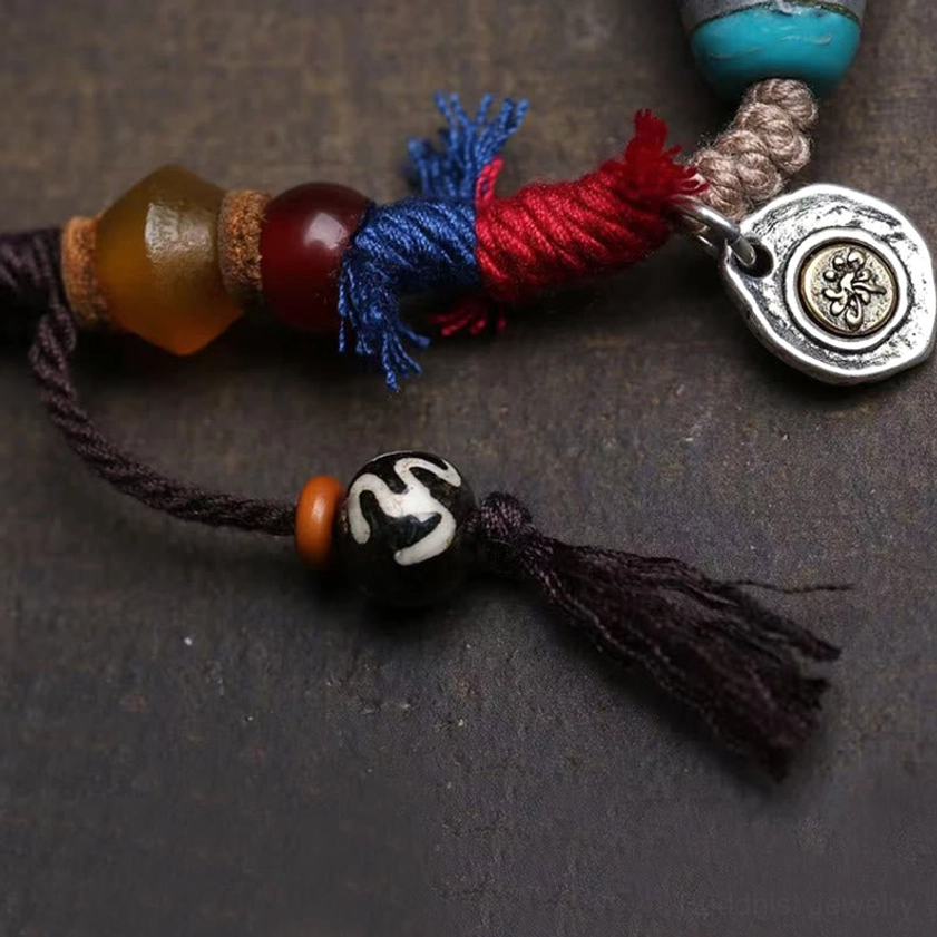 Buddhist necklace overhead view showing mini dzi bead, silver brand charm, and black tassel decoration on accessories