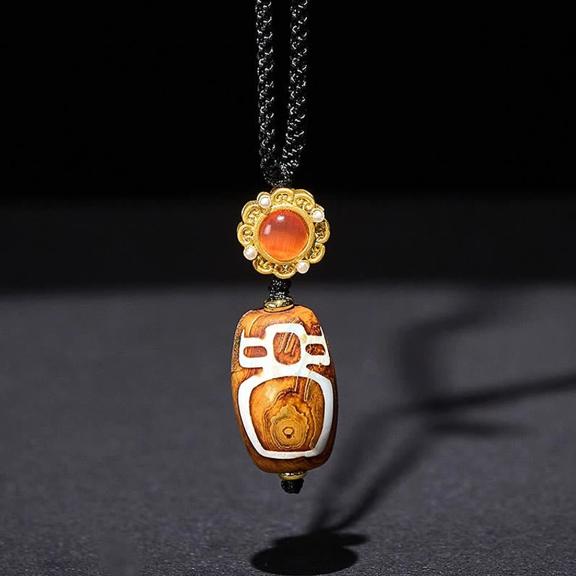 Hand-carved Buddhist nine-eye dzi bead pendant with natural brown agate and white pattern on grey studio background