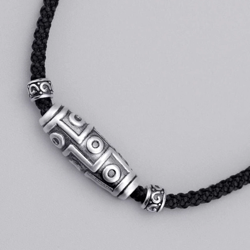 Side profile of sterling silver nine-eye dzi bead necklace highlighting geometric carved patterns and black braided rope
