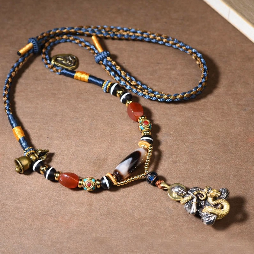 Snake Buddha pendant necklace front view showing hand-painted dzi bead and woven cord on brown wooden background