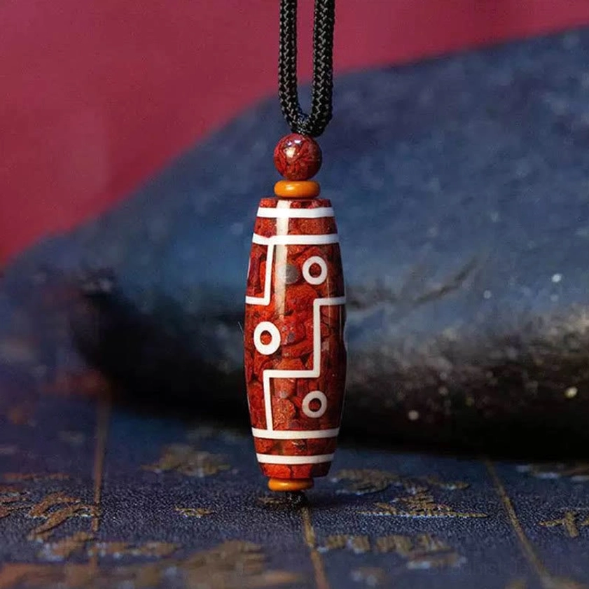 Nine-eye dzi bead necklace with white line patterns and black rope, laid flat on dark stone background, showcasing traditional Buddhist spiritual jewelry