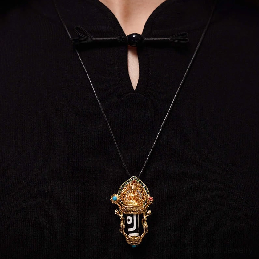 Worn Dzi Bead pendant necklace on person wearing black traditional shirt, close-up view of single-eye Dzi in gold setting with black wax cord
