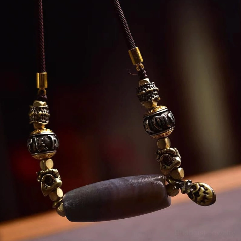 Close-up side view of Buddhist necklace pendant featuring grey agate Dzi bead with dual-tone metal charms and bell accent