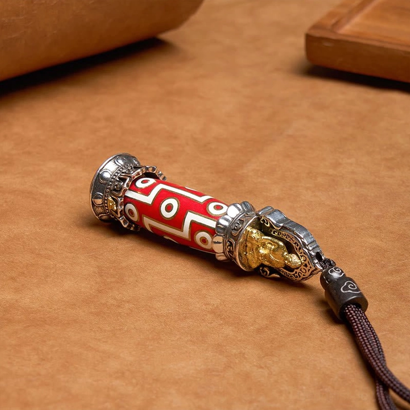 Handcrafted Nine-Eye Dzi healing pendant with gold Buddha cap and geometric red-white design in flat lay presentation