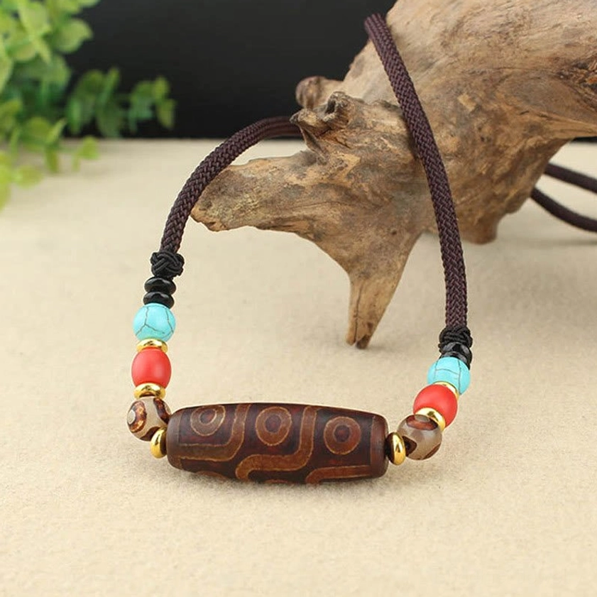 Low angle side view of hand-painted dzi bead pendant necklace with braided brown cord and metal spacer accents