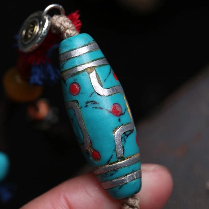 Close-up handheld view of turquoise dzi bead pendant with silver inlay and silver brand charm on braided cotton rope