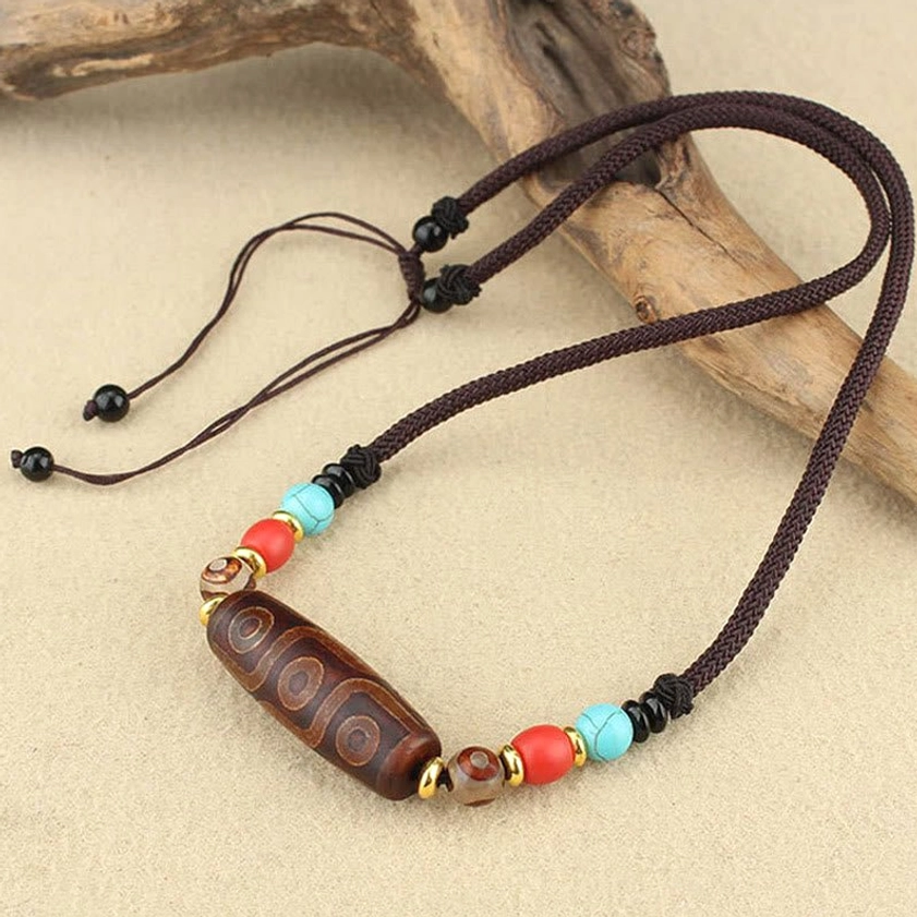 Side view of dzi bead Buddhist protection necklace with adjustable pull-string cord and colorful stone spacers on wooden surface