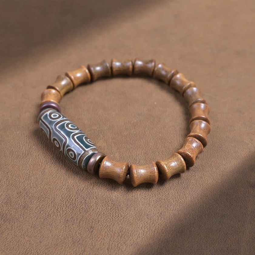 Nine-eye dzi bead bracelet with cylindrical sandalwood beads on brown fabric background