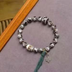 Dzi bead skull bracelet with black and white patterned beads, resin skull accent, and green tassel on purple fabric background