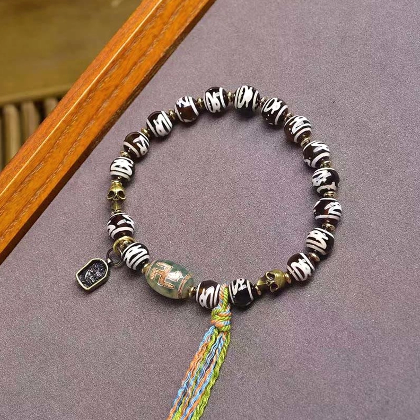 Dzi bead wealth bracelet with black and white beads, green agate stone, colorful woven tassel, and square metal prosperity charm