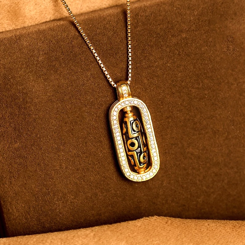 Nine-eye dzi wealth pendant necklace featuring polished gold box chain and CZ-encrusted rectangular frame on suede fabric