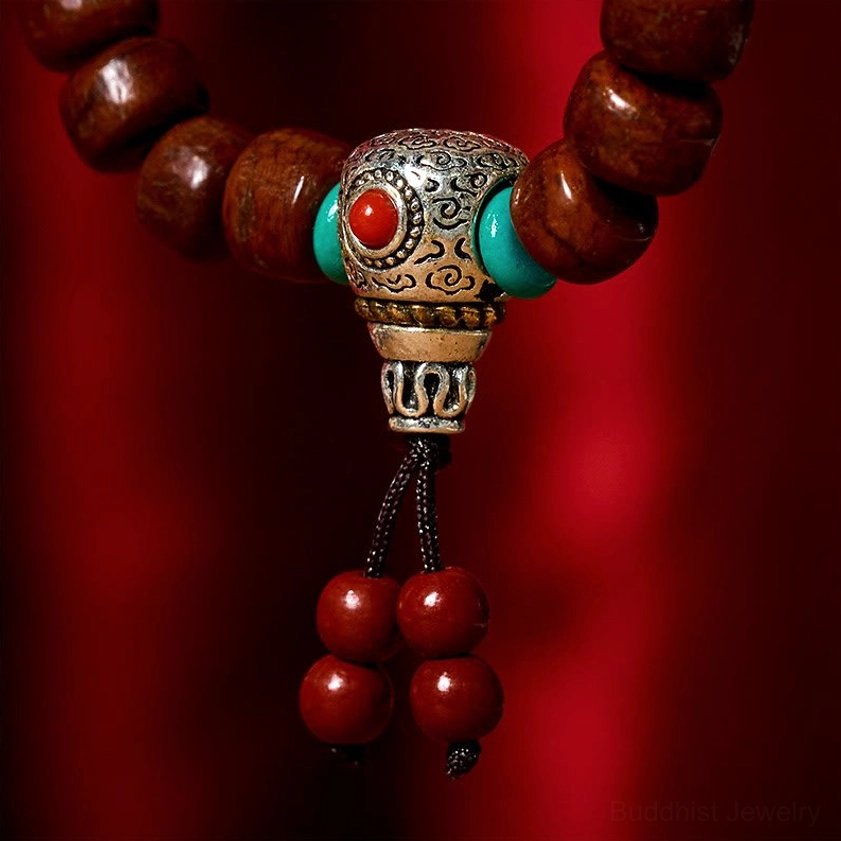 Macro close-up of Dzi bracelet center clasp featuring carved silver bead with turquoise and red stone accents and red tassel