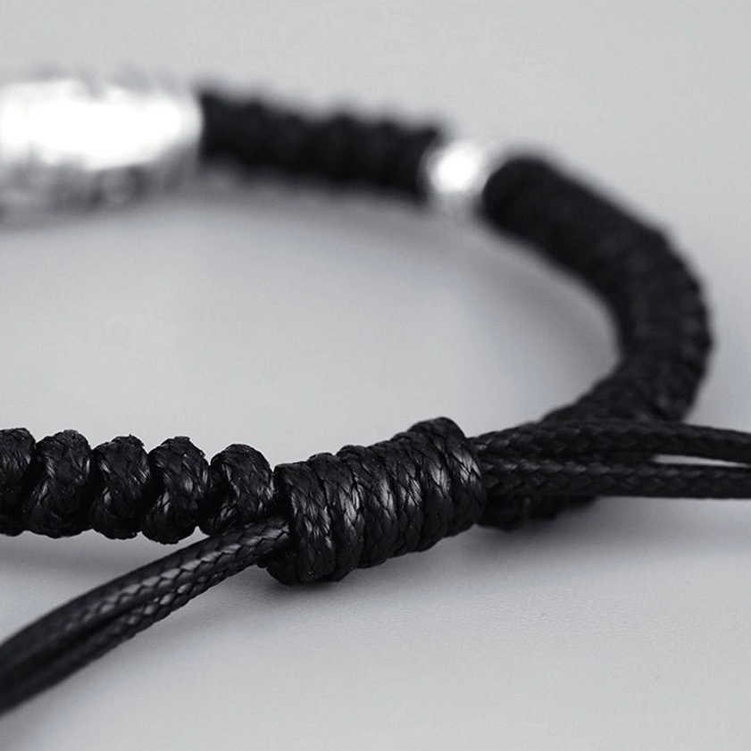Detailed close-up of black braided wax cord knot work and engraved silver spacer beads on nine-eye dzi bracelet