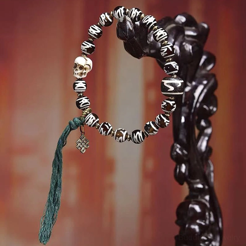 Dzi bead skull bracelet displayed on wooden stand showing skull bead, dzi beads, and green tassel accent