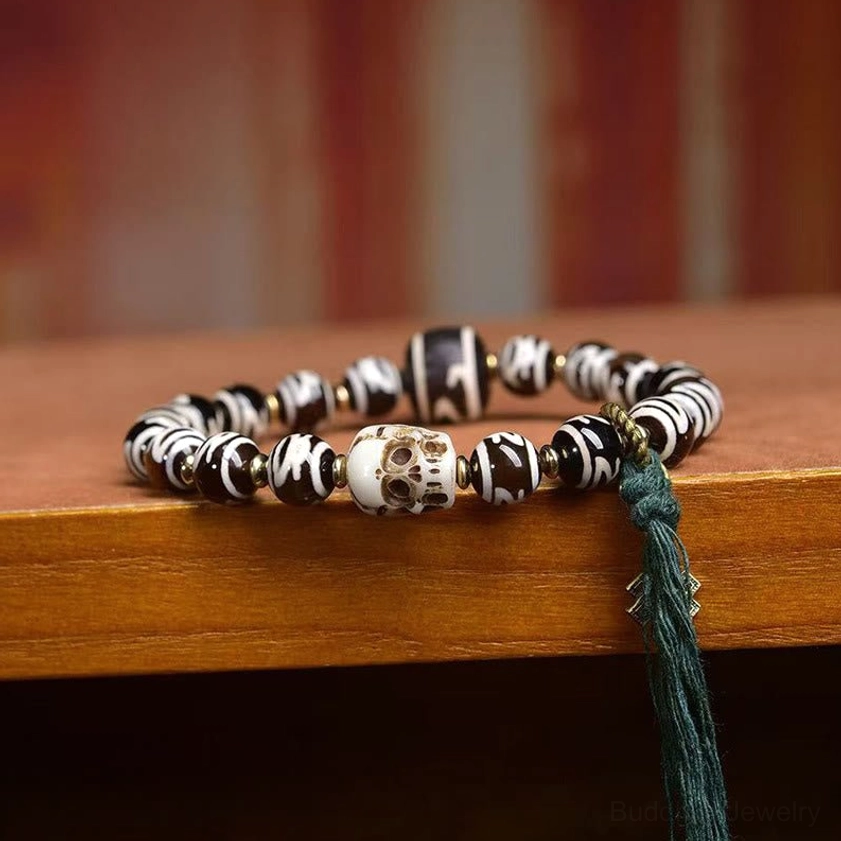 Side view of dzi bead skull bracelet featuring multiple hand-painted dzi beads, large resin skull, and green tassel