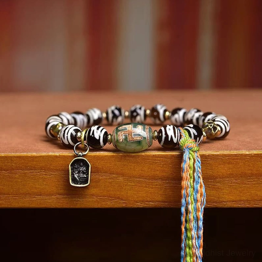 Side view of dzi bead wealth bracelet showing green agate dzi beads, enamel metal charm, and colorful woven tassel