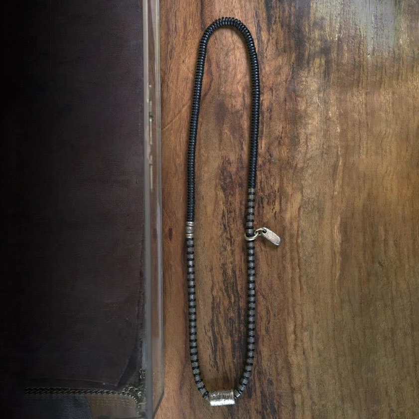 Ebony wood beaded bracelet strand coiled on wooden surface with antique copper clasps and hardware detail