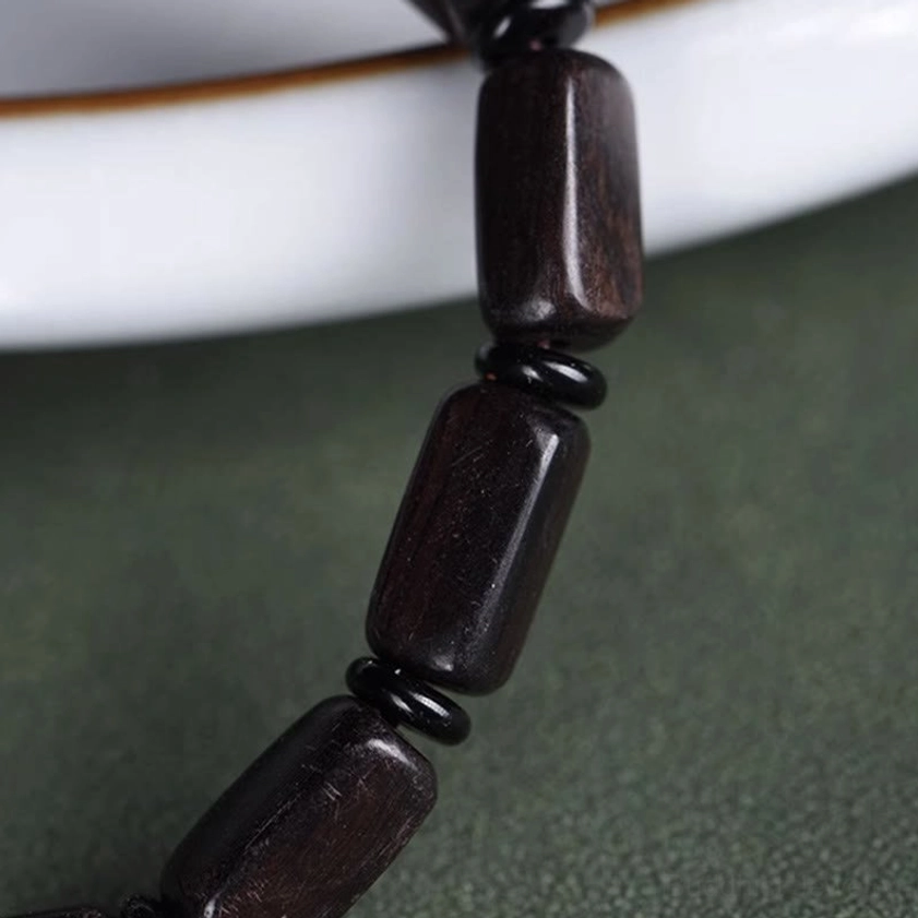 Detailed side view extreme close-up of polished ebony wood rectangular beads and black spacer rings on ceramic background