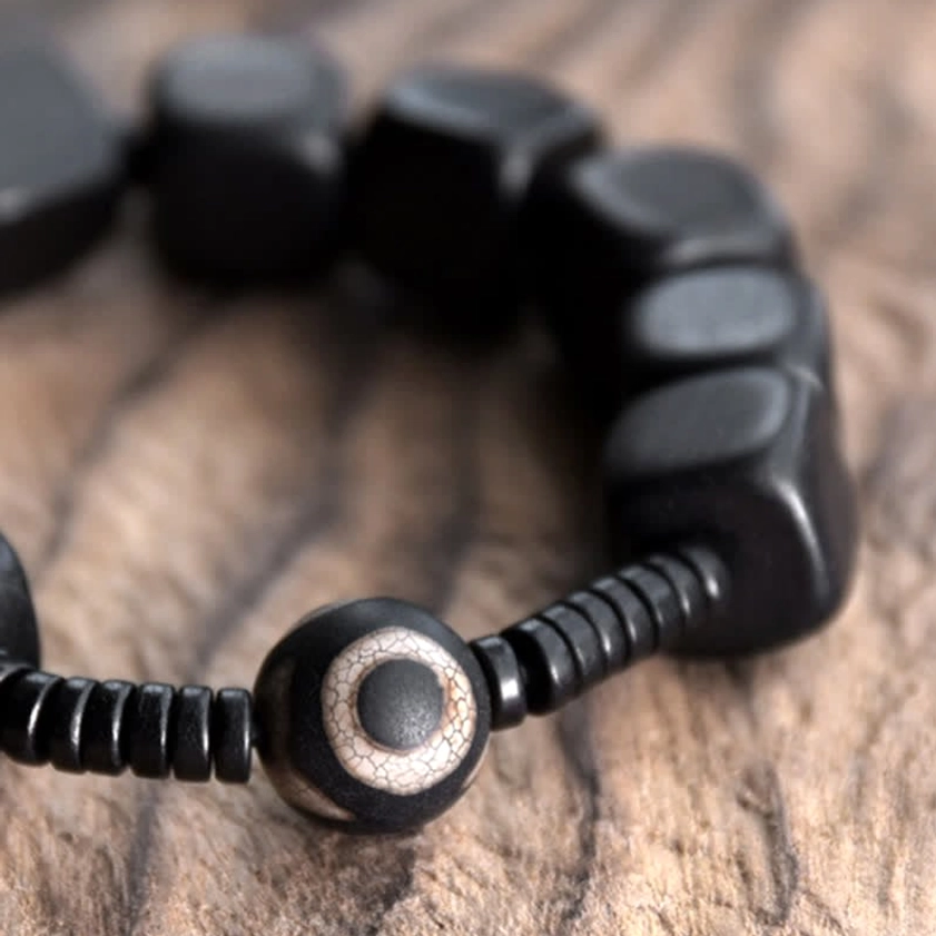 Ebony wood dzi bracelet in macro close-up, displaying square ebony beads and round eye spiritual amulet
