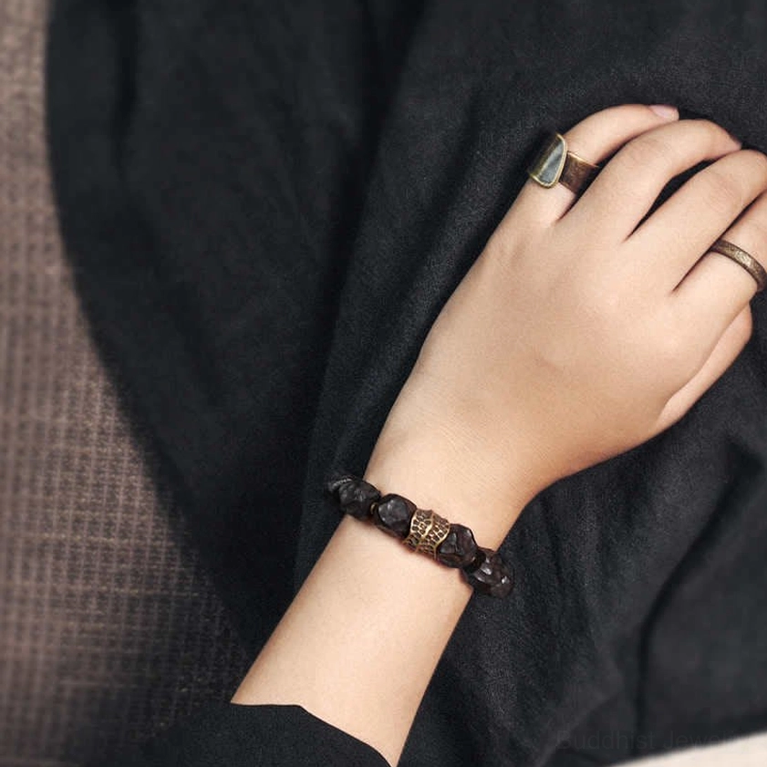 Close-up detail of ebony wood copper bracelet worn on hand showing black matte beads with bronze metal accents