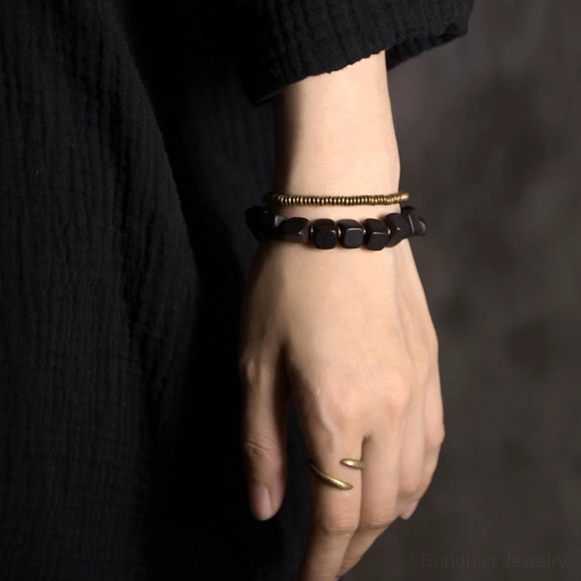 Double wrap Buddhist bracelet being worn on hand and wrist with gold finger ring and black clothing background