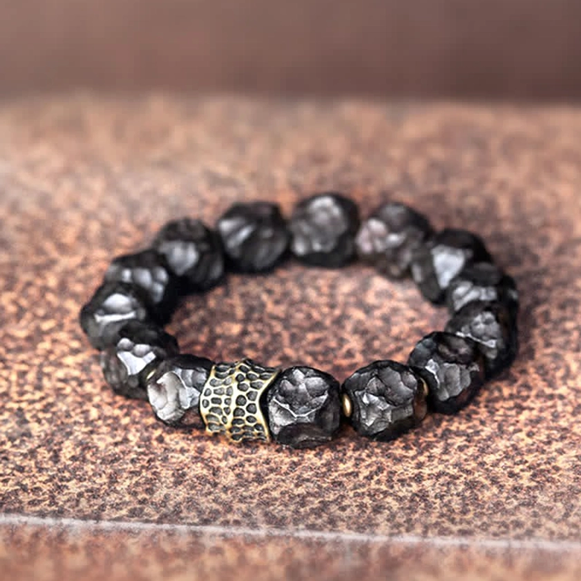 Irregular hammered ebony wood beads with bronze metal components on brown leather, showing handcrafted texture