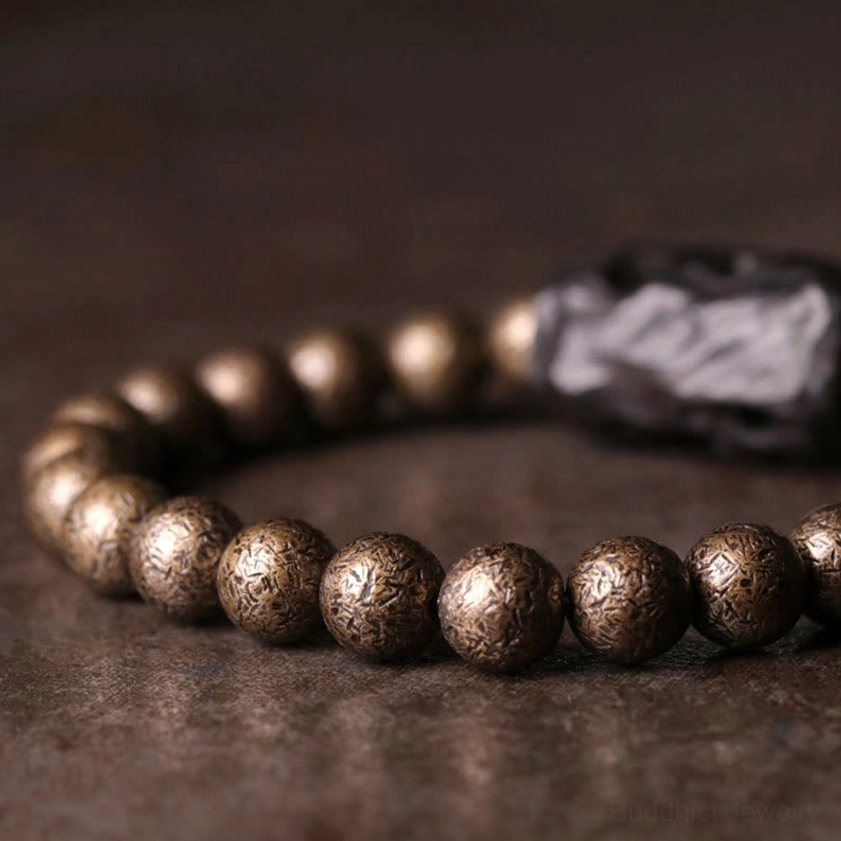 Partial view of ebony and copper beaded bracelet showing textured bronze beads and rough carved ebony wood spacer on dark background