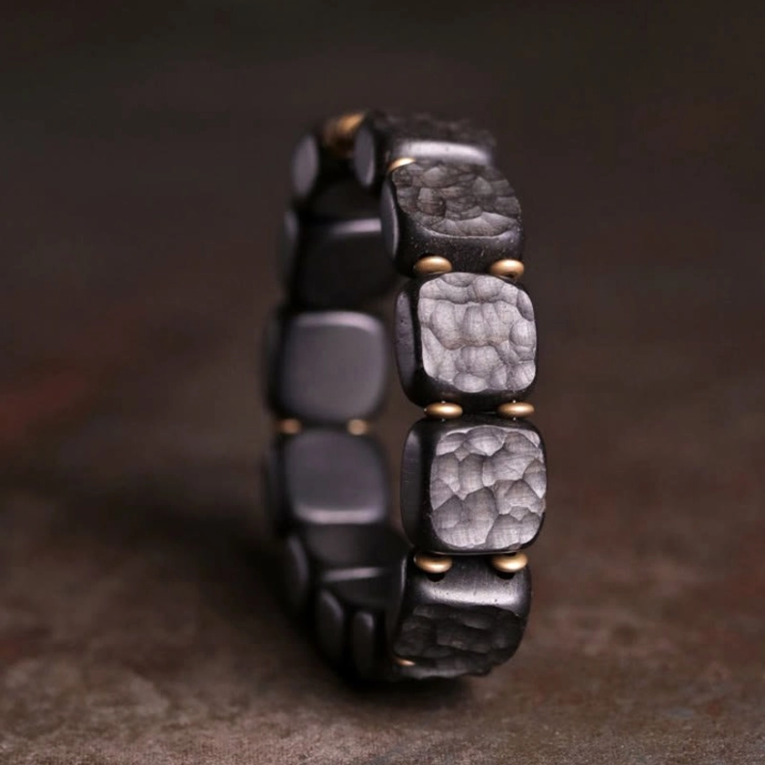 Close-up side view of handcrafted ebony and copper bracelet showing stacked square beads with metal connector details