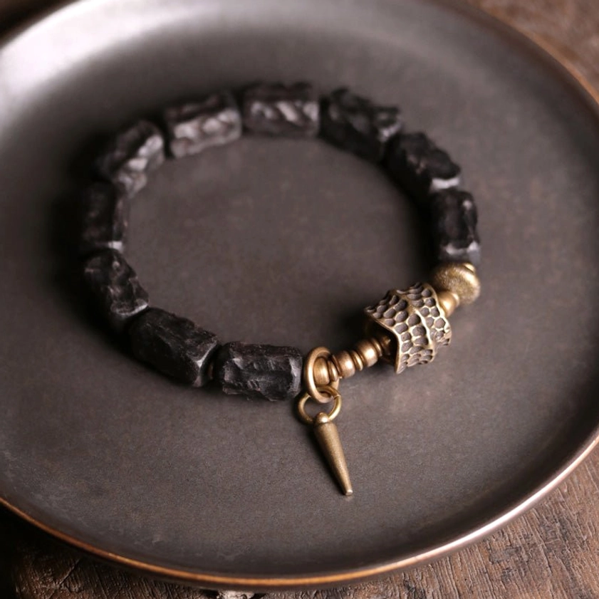 Buddhist protection bracelet with ebony wood and copper hardware displayed on dark metal surface showing spike pendant detail