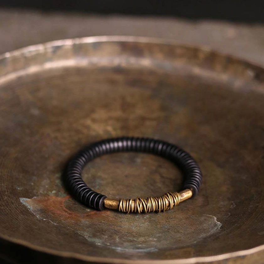 Ebony wood and copper Buddhist bracelet worn on wrist displayed on vintage metal serving tray, showing compact comfortable fit