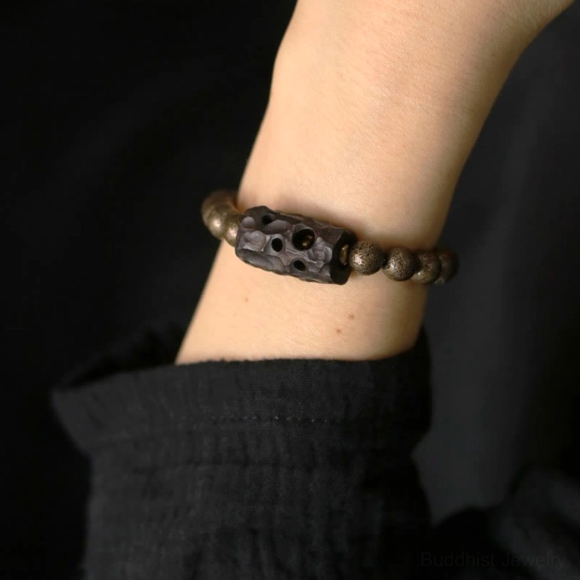 Slim fitting ebony wood copper Buddhist bracelet on wrist with minimalist retro design and dark clothing backdrop