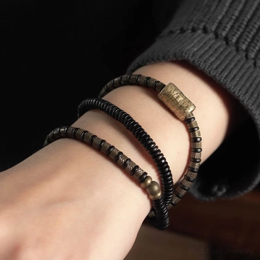 Ebony wood Buddhist healing bracelet worn on wrist close-up side view with dark knit sleeve background