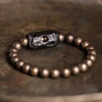 Ebony wood and copper Buddhist bracelet flat lay on rustic wood surface with detailed view of antiqued bronze beads and carved hollow ebony spacer