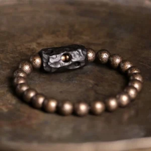 Ebony wood and copper Buddhist bracelet flat lay on rustic wood surface with detailed view of antiqued bronze beads and carved hollow ebony spacer