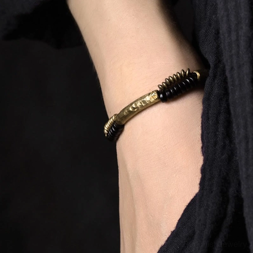 Worn ebony wood and copper Buddhist bracelet on wrist showing casual daily styling with slim fit on dark fabric background