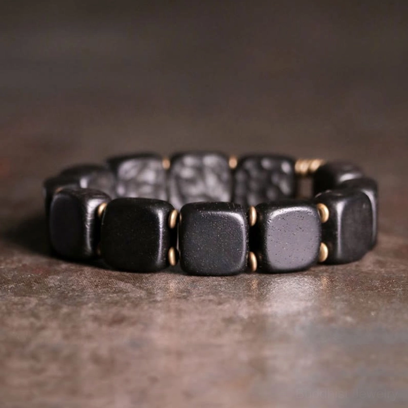 Polished ebony wood and antique copper bracelet with smooth and textured square beads on rustic background