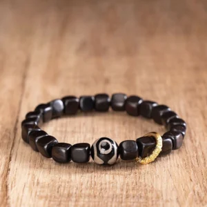 Ebony wood and nine-eye dzi bead bracelet for protection, shown from overhead angle on wooden surface with gold-tone metal accent ring