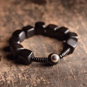 Ebony wood dzi bead bracelet with nine-eye charm and black spacers, flat lay overhead view on vintage wooden surface