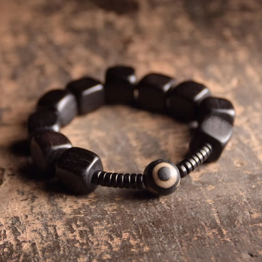 Ebony wood dzi bead bracelet with nine-eye charm and black spacers, flat lay overhead view on vintage wooden surface