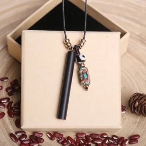 Ebony wood dzi bead Buddhist necklace pendant displayed with gift box, red beans, and natural elements on wooden surface