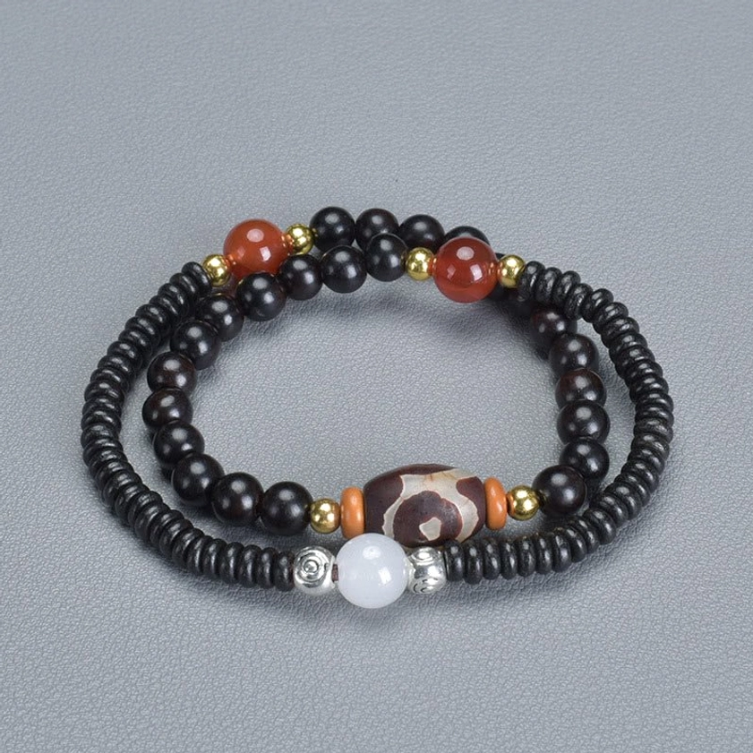 Oblique overhead view of ebony wood and red agate dzi bead double wrap bracelet on gray fabric with detailed bead visibility