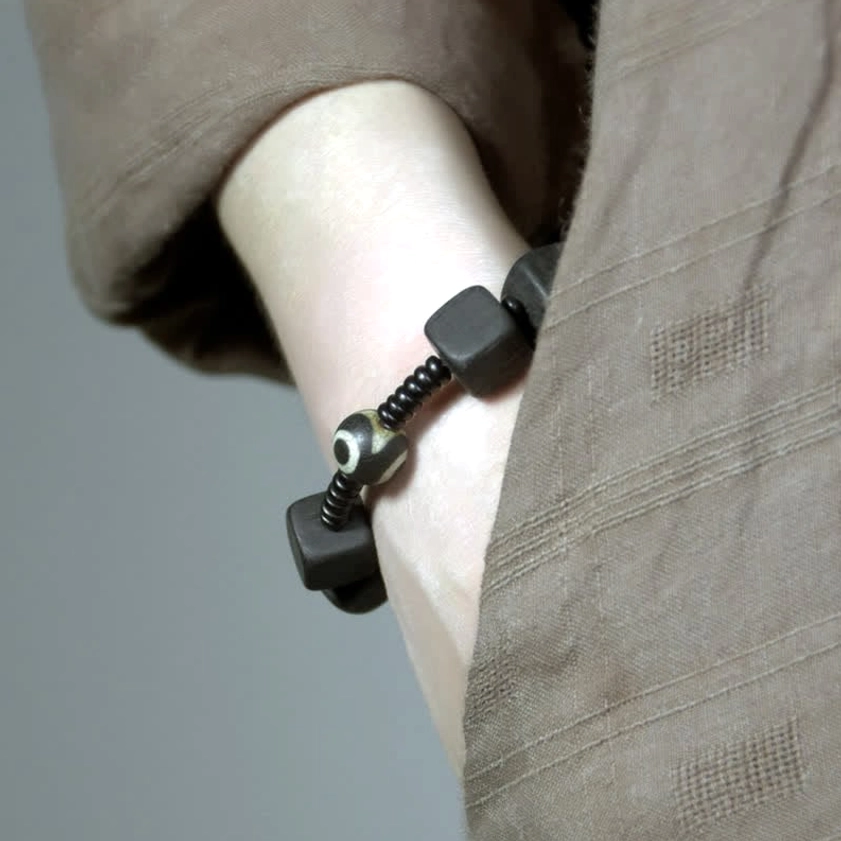 Nine-eye dzi bead bracelet worn on wrist, showing dark ebony beads and protective spiritual charm in close-up detail