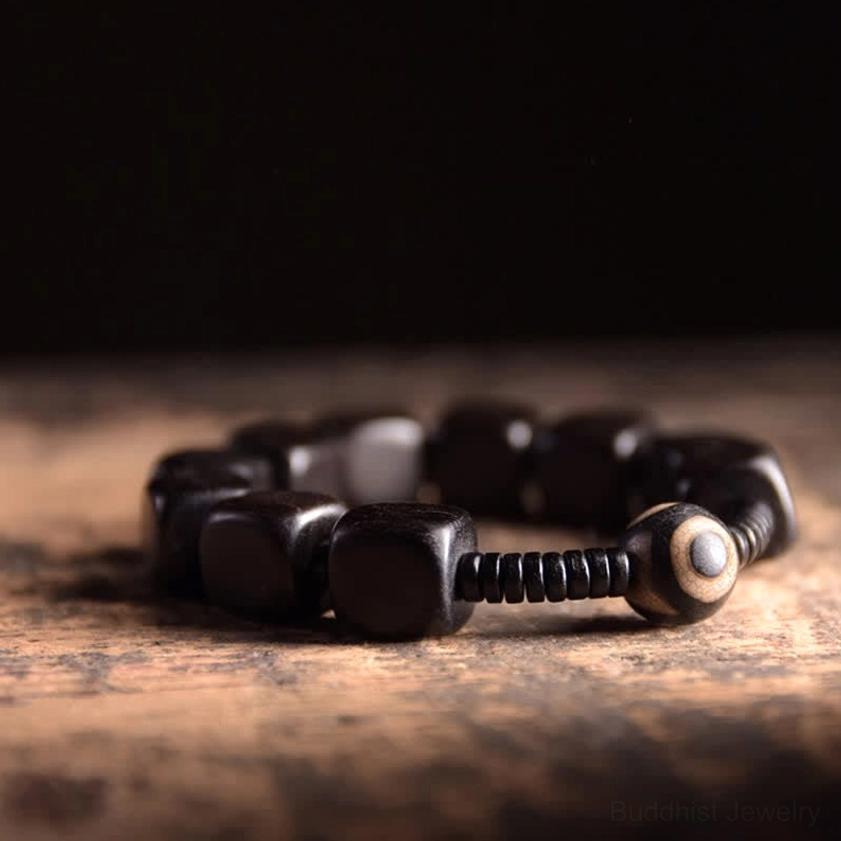 Dark ebony wood dzi bracelet with polished beads and one-eyed spiritual charm on rustic wooden workbench