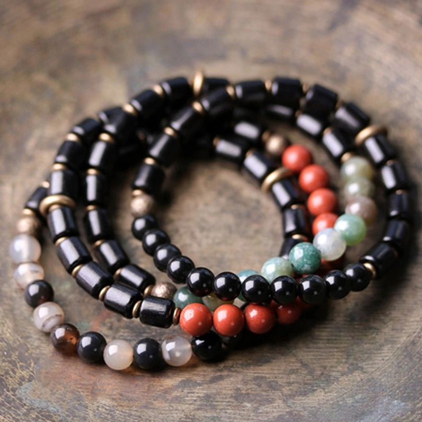 Multiple stacked ebony wood and gemstone Buddhist bracelets coiled together on vintage wooden background displaying collection