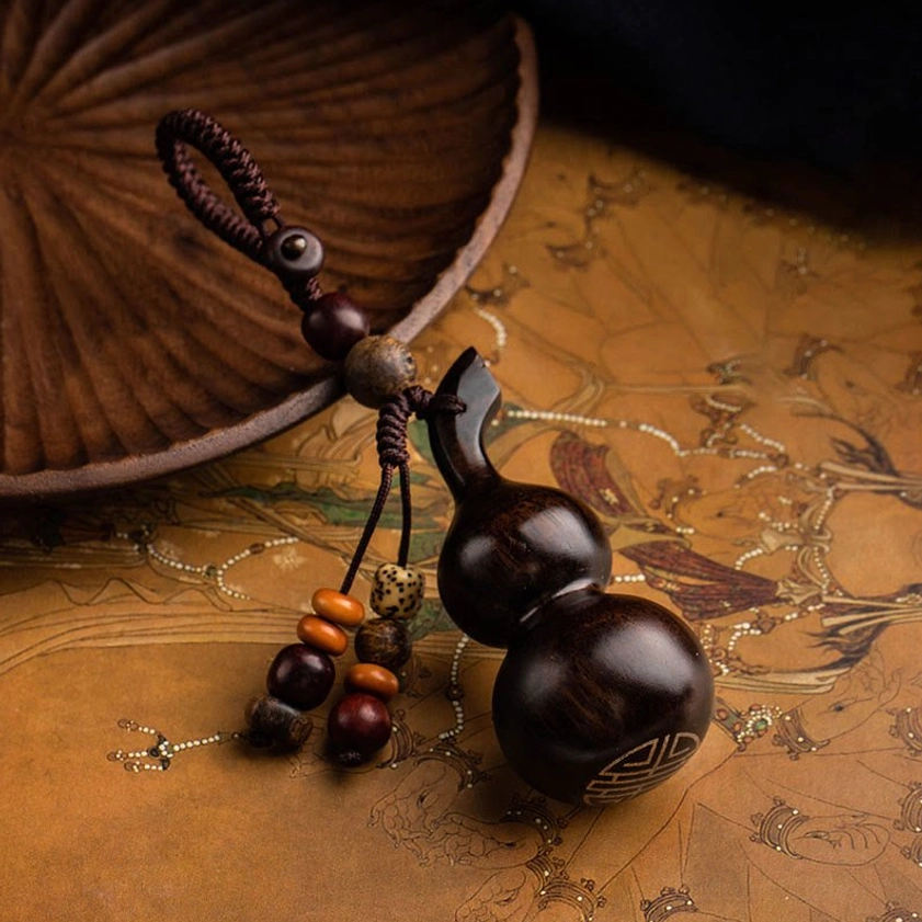 Dark ebony gourd keychain flat lay on antique map with wooden tray, featuring hand-engraved protection symbol and braided rope attachment