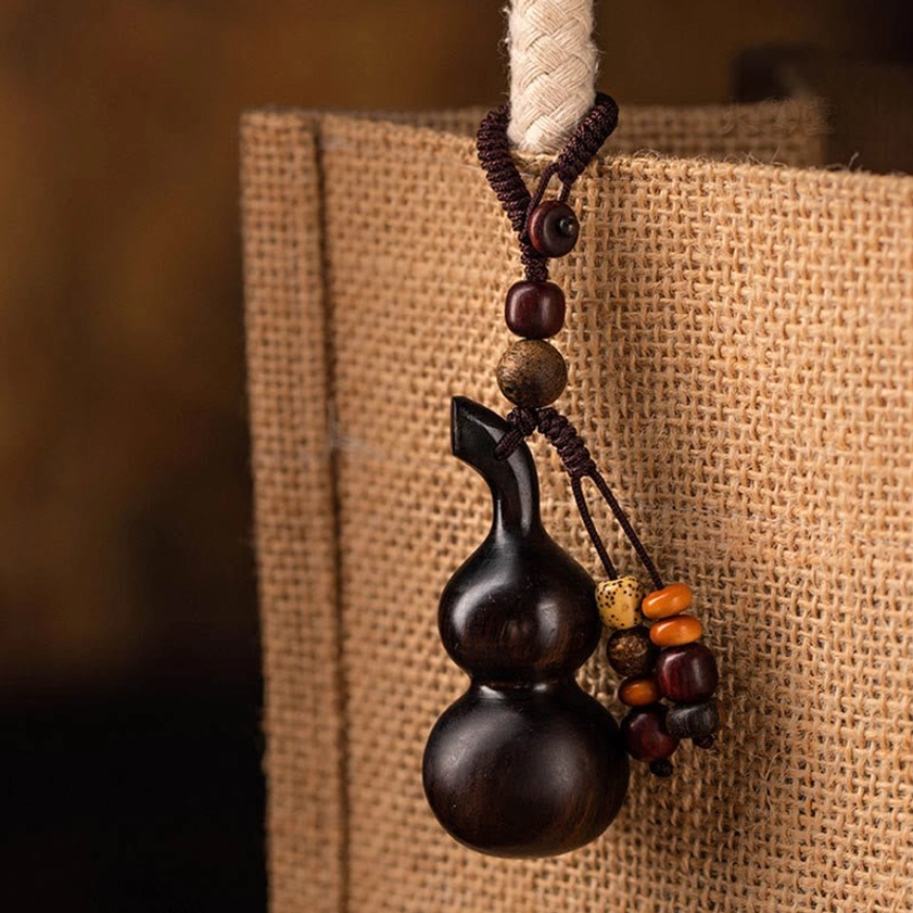 Close-up of ebony gourd Buddhist keychain hung on burlap tote bag, displaying mixed beaded tassel decorations and natural wood patina for spiritual protection