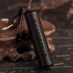 Ebony wood Heart Sutra Buddhist keychain with engraved scripture, braided cord, and black bead detail—close-up front view on wooden base