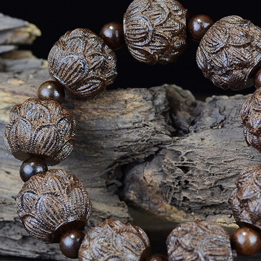 Close-up oblique view of ebony lotus carved Buddhist bracelet on weathered wood, emphasizing intricate lotus flower carving details
