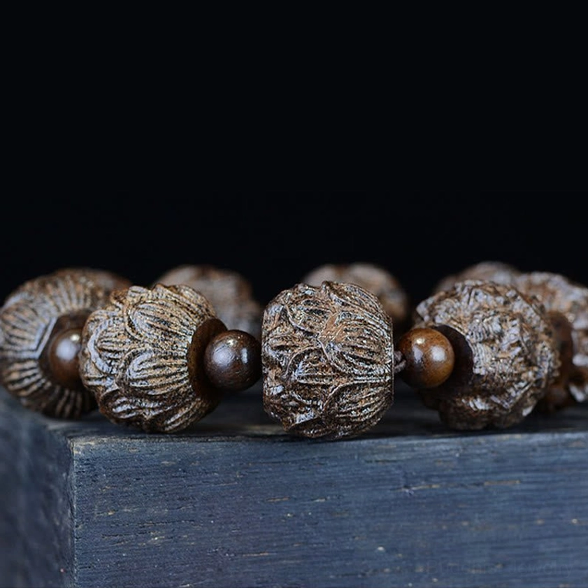 Ebony lotus bracelet flat lay on dark wooden block surface, showcasing embossed lotus bead details and brown spacer beads